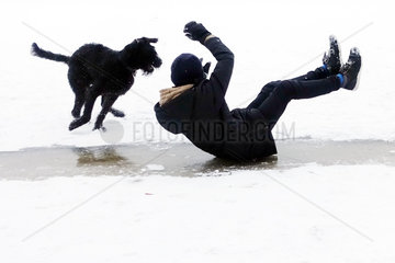 Berlin  Deutschland  Junge rutscht in Begleitung seines Hundes auf dem Hosenboden ueber eine Eisflaeche