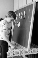 Berlin  DDR  Junge klebt in der Vorschule Figuren aus Papier an eine Tafel
