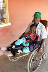Kenia  ein behinderter Junge liegt in den Armen eines in einem Rollstuhl sitzenden