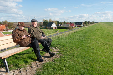 Kaiser-Wilhelm-Koog  Deutschland  zwei Senioren sitzen auf dem Deich auf einer Bank und schauen auf die Nordsee