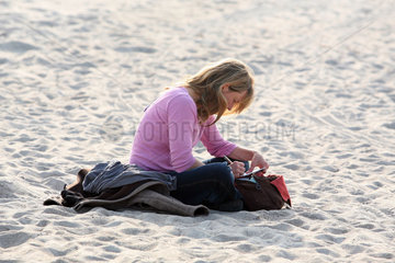 Warnemuende  eine Frau sitzt am Strand und schreibt einen Brief