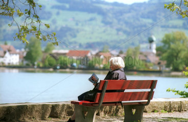 Rentnerin liest auf einer Bank am Bodensee  Schweiz