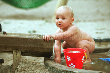 Kleinkind (12 Monate) spielt nackt im Sandkasten  Berlin
