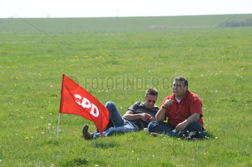 Brunsbuettel  Deutschland  zwei Maenner mit SPD-Fahne sitzen auf einer Wiese