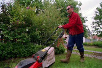 Mann beim Rasenmaehen in einem Garten