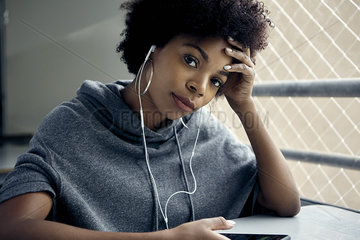 Young woman listening to earphones  holding head  portrait