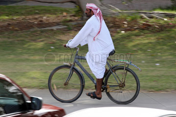 Dubai  Mann in Landestracht faehrt Fahrrad