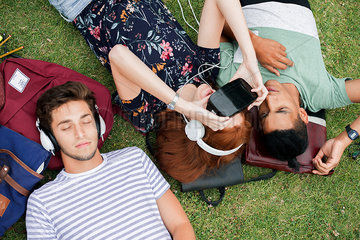 Friends lying on grass  using virtual reality simulator and listening to headphones