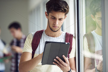 Male college student using digital tablet in corridor