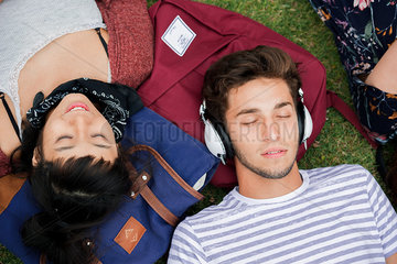 Young man lying on grass with friends  listening to headphones