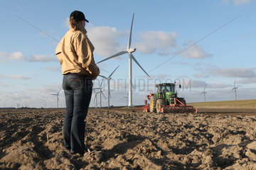 Reussenkoege  Deutschland  eine Frau beobachtet wie ein Landwirt im Fruehling die Saat ausbringt