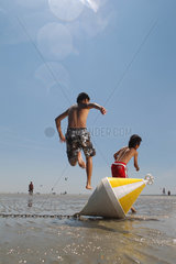 St. Peter-Ording  Deutschland  zwei Kinder springen am Strand bei Niedrigwasser ueber eine Positionstonne