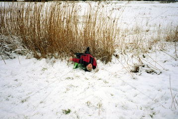 Junge liegt am Ende einer Schlittenfahrt im Schnee