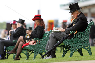 Ascot  Grossbritannien  elegant gekleidete Menschen sitzen auf Baenken