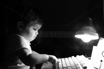 Spanien  kleines Maedchen tippt abends auf einer PC-Tastatur