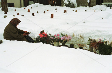 Sarajevo  Bosnien und Herzegowina  Frau sitzt im Schnee an einem Grab