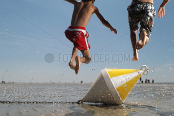 St. Peter-Ording  Deutschland  zwei Kinder springen am Strand bei Niedrigwasser ueber eine Positionstonne