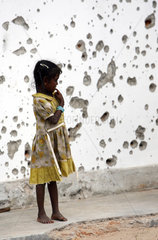 Vakarai  Sri Lanka  Kind steht allein vor einer zerschossenen Haeuserwand