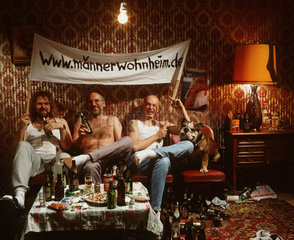 Hamburg  Deutschland  Maenner sitzen auf einem Sofa  trinken Bier und halten ein Transparent