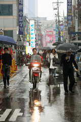Seoul  Fussgaenger und Motorradfahrer auf regennasser Strasse