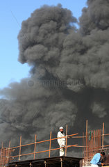 Dubai  Vereinigte Arabische Emirate  Bauarbeiter steht auf einem Geruest vor einer schwarzen Rauchwolke