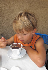 Berlin  Deutschland  Junge loeffelt lustlos in einer Tasse mit Kakao