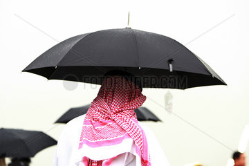 Dubai  Vereinigte Arabische Emirate  Mann in Landestracht steht unter einem Regenschirm