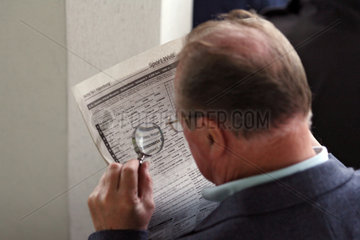Hamburg  Deutschland  Mann liest seine Zeitung mit Hilfe einer Lupe