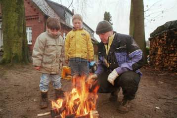 Vater zeigt seinem Sohn und Nachbarjungen den Umgang mit Feuer  Norddeutschland