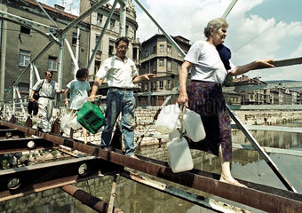 Sarajevo  Bosnien und Herzegowina  Menschen mit Taschenund Wasserkanistern ueberqueren den Miljacka