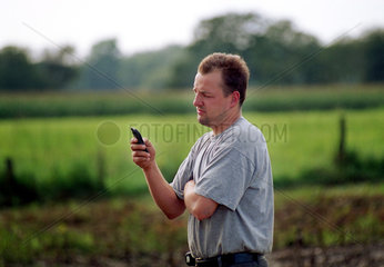 Junger Landwirt mit Handy auf dem Feld