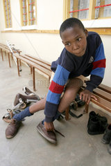 Kenia  ein behinderter Junge bindet sich seine Schuhe zu