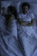 Man lying awake in bed next to sleeping wife
