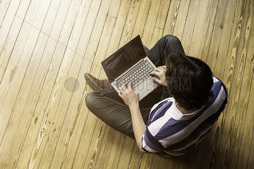 Man sitting indian style on floor using laptop computer