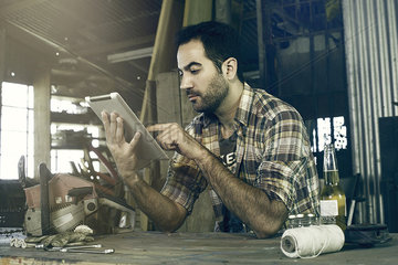 Man in workshop using digital tablet to access do-it-yourself repair instructions on internet
