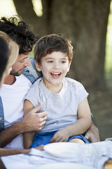 Little boy sitting on father's lap at outdoor meal