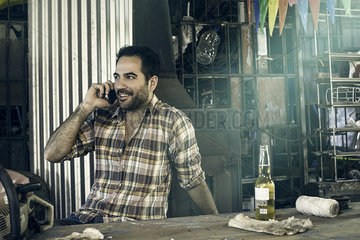 Man having beer and chatting on phone in workshop