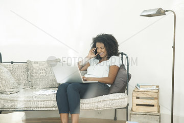 Woman chatting on cell phone and using laptop computer at home