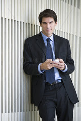 Businessman leaning against wall  using smartphone