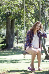 Young woman sitting on park swing with sad expression on face