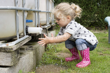 Little girl washing hands under outdoor cistern spigot