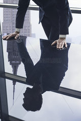 Businessman leaning against table  reflection in glass top