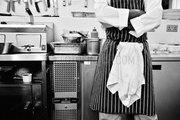 Chef with arms folded standing in commercial kitchen  mid section