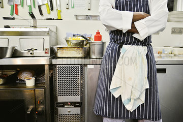 Chef standing in commercial kitchen with arms folded  mid section