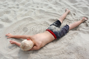 Ein kleiner Junge liegt im Sand