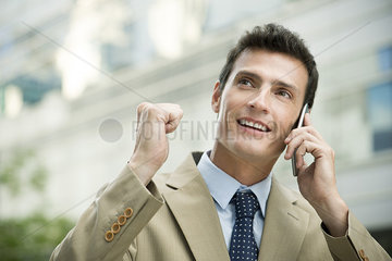 Businessman celebrating good news while talking on cell phone