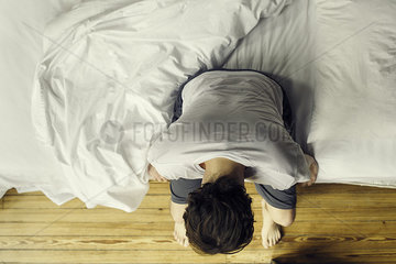 Man sitting on edge of bed holding head