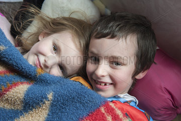 Young siblings lying under blanket together  portrait