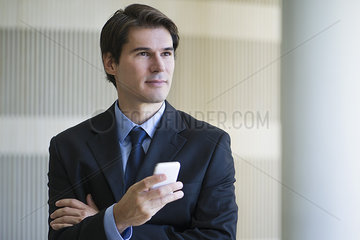 Businessman holding smartphone  looking away in thought