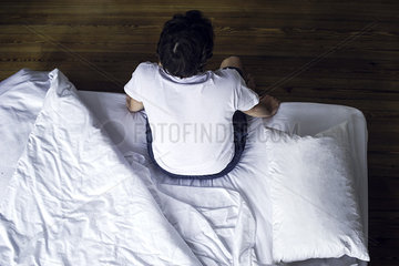 Man sitting on edge of bed waking up